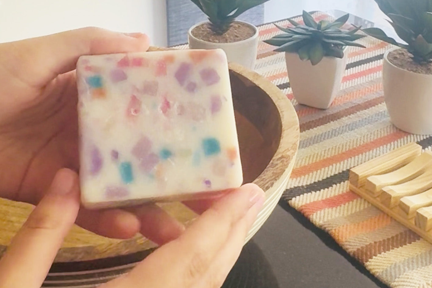 Hand holding a colorful soap bar with a blurred indoor setting